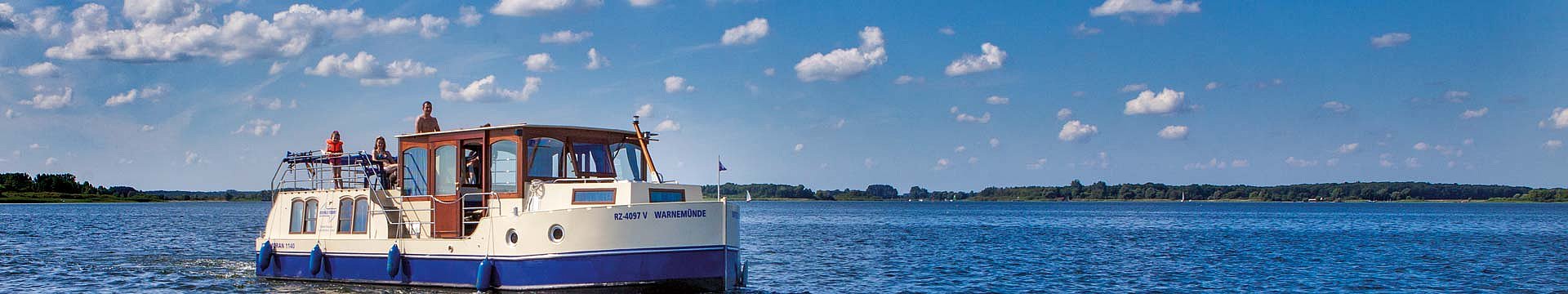 Ein Ehepaar mit Kind fährt auf dem Hausboot Kormoran über einen tiefblauen See.